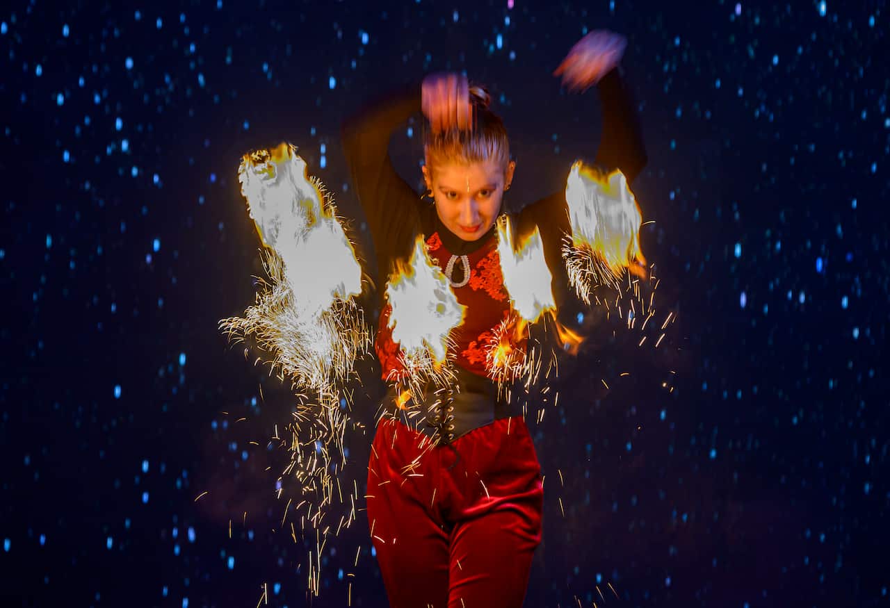 An artist in red performs with sparkly fire displays