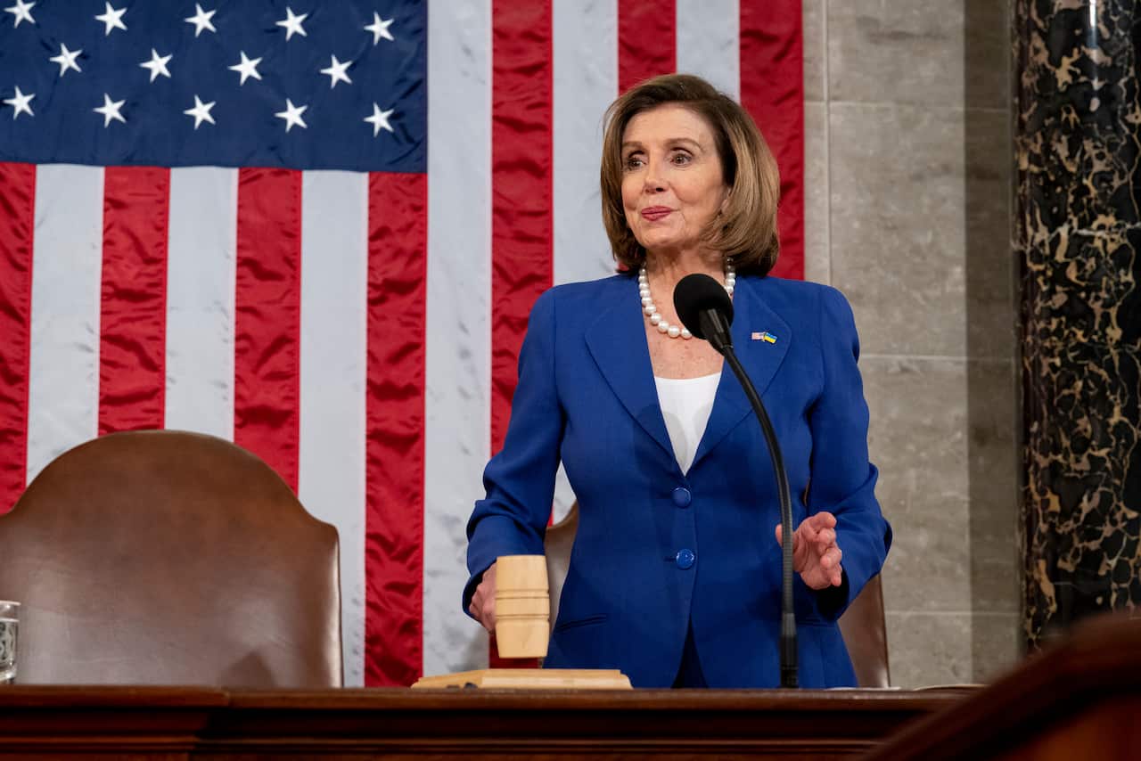 A woman in a blue suit banging a gavel at a desk in front of a US flag.