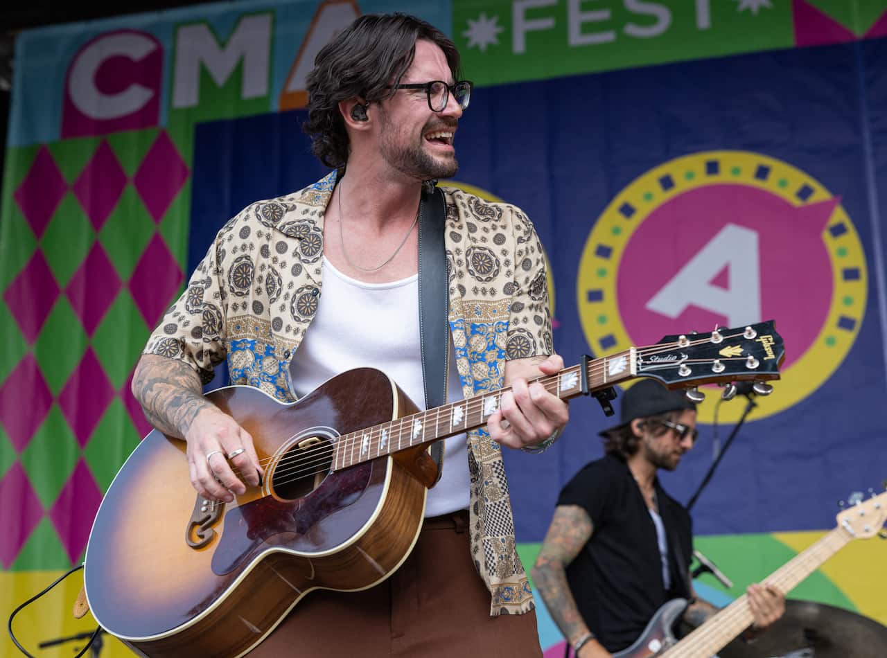 A man is holding an acoustic guitar performing at a festival