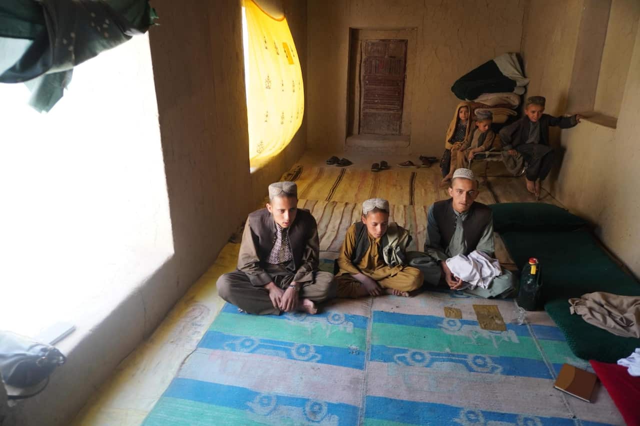 Three Afghan boys sit on a rug.