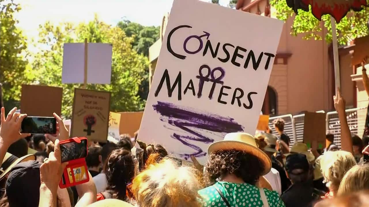 People hold up a sign that says, 'consent matters'. 