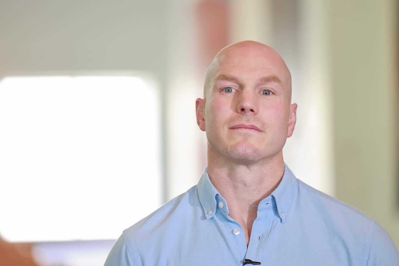 A man in a blue shirt looks seriously off camera. 