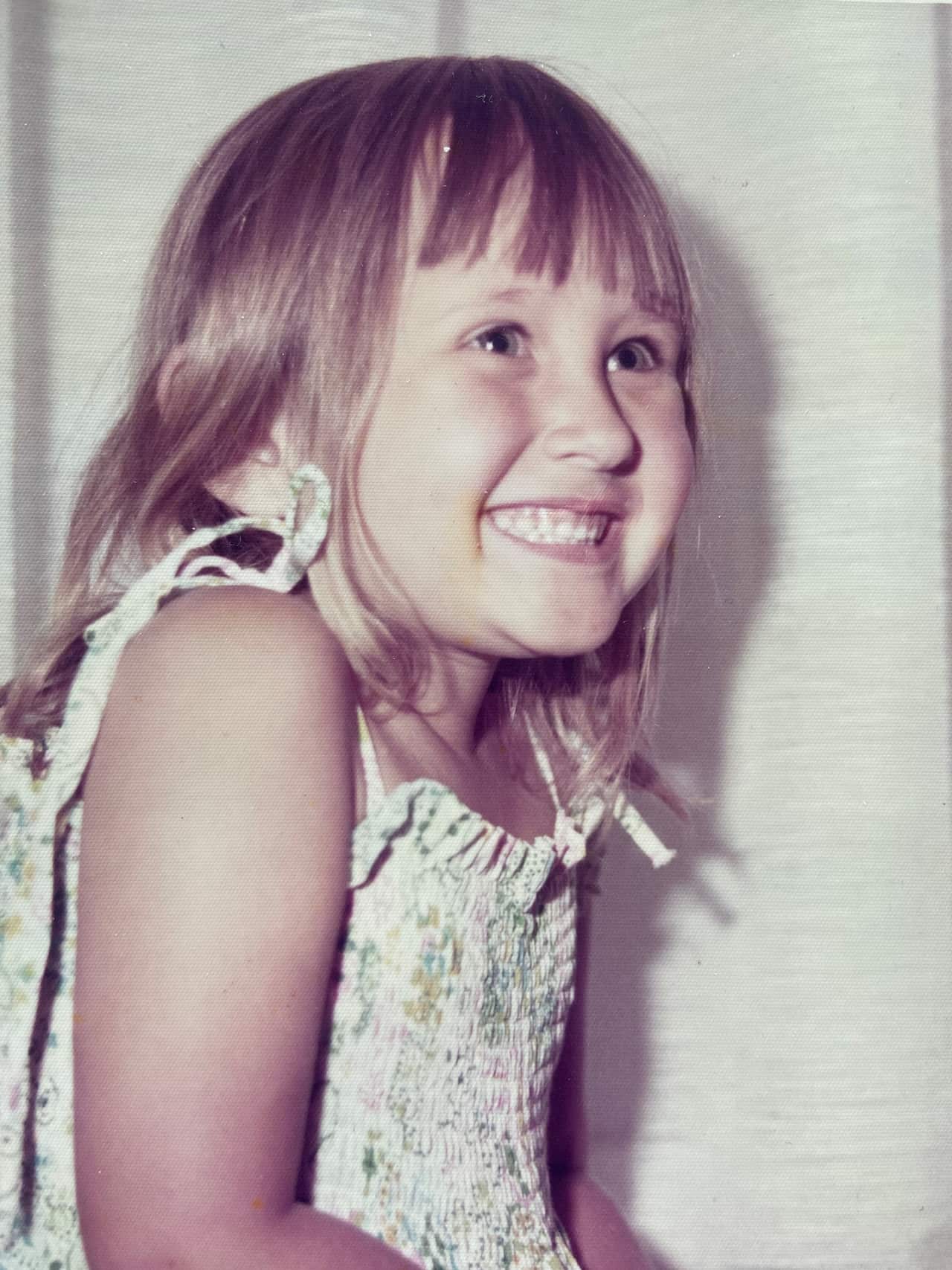 a young blonde girl in a white dress smiles looking away from the camera