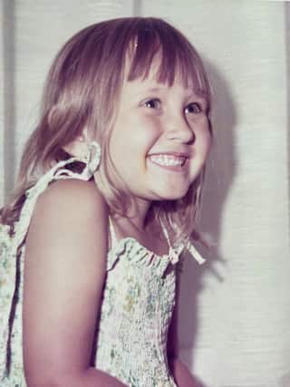 a young blonde girl in a white dress smiles looking away from the camera