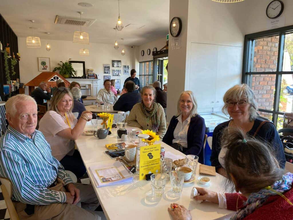 Patrons sitting at a long table at a Chatty Cafe.