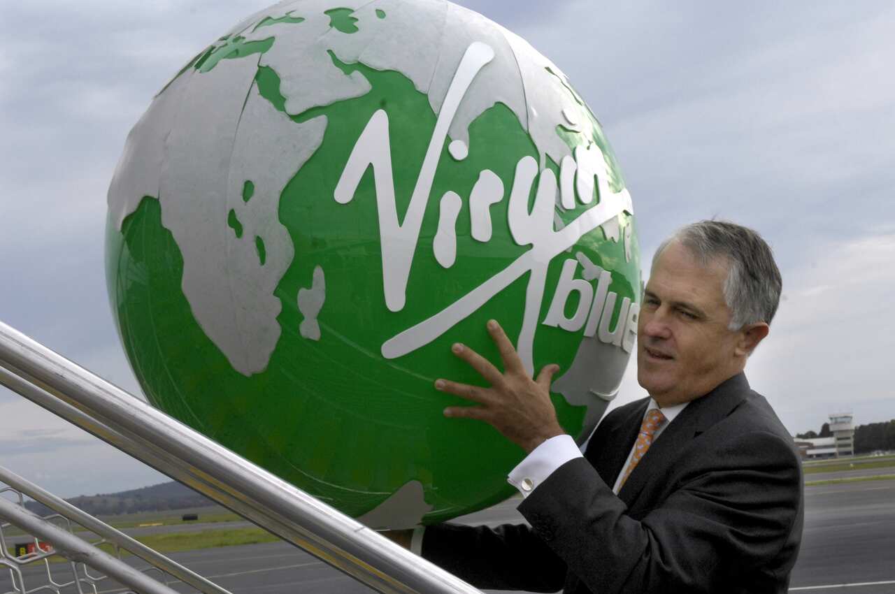 Malcolm Turnbull heads up a set of aeroplane stairs holding up a large green globe with 'Virgiin blue' written on it.