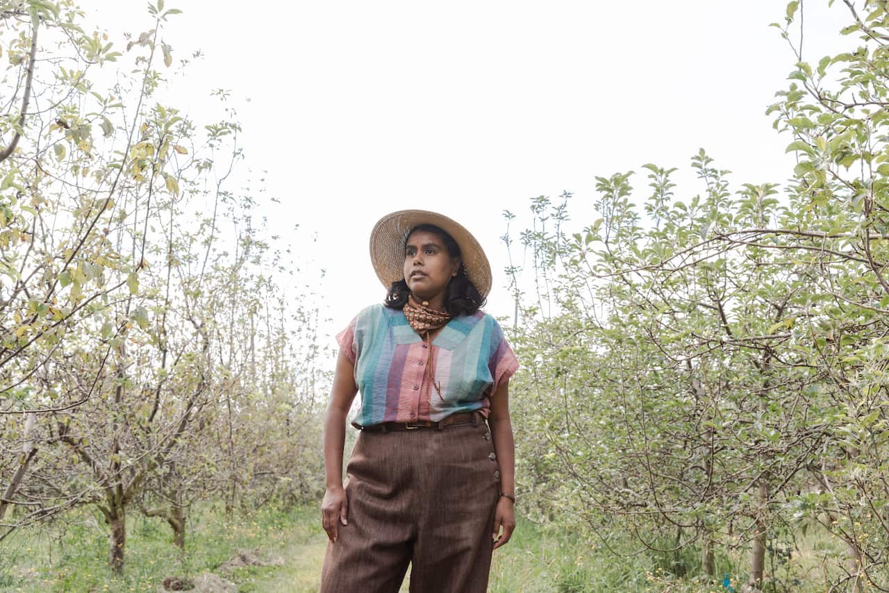 A woman stands in the middle of an apple orchard looking beyond the camera
