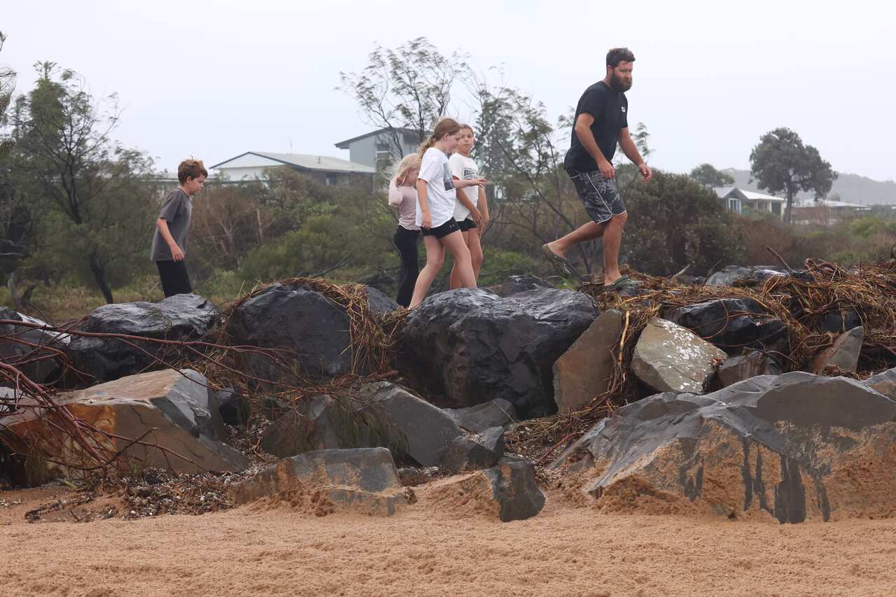 A group of people walk on the rocks near a beach.