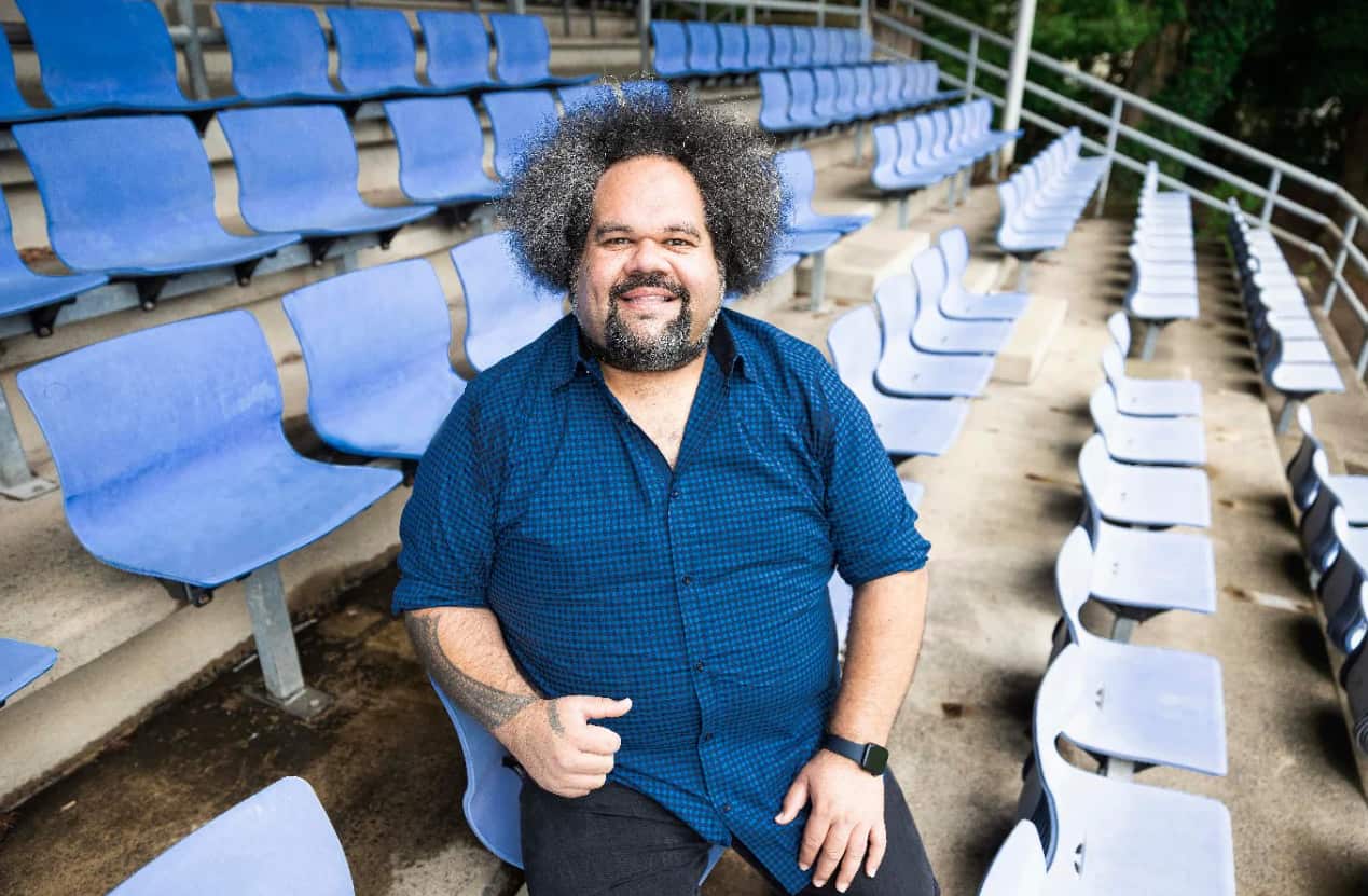 Jioji sits in the bleachers with a blue shirt on