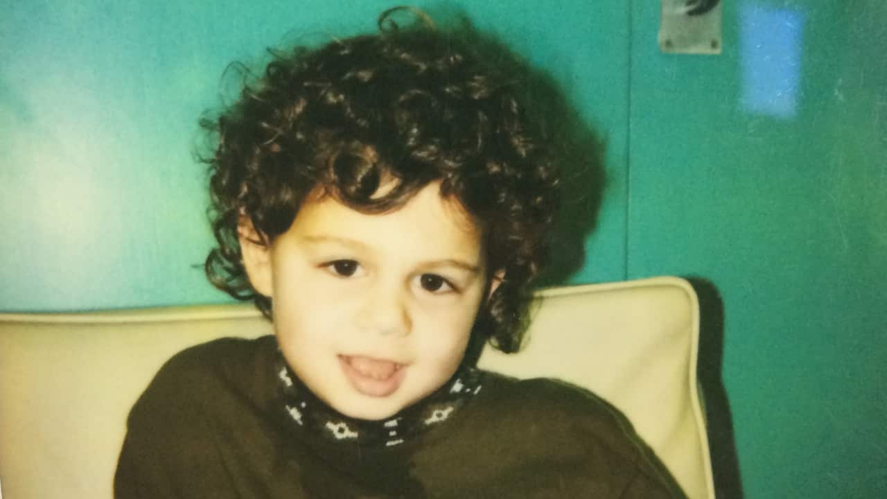 a young boy with curly dark hair sitting on a couch