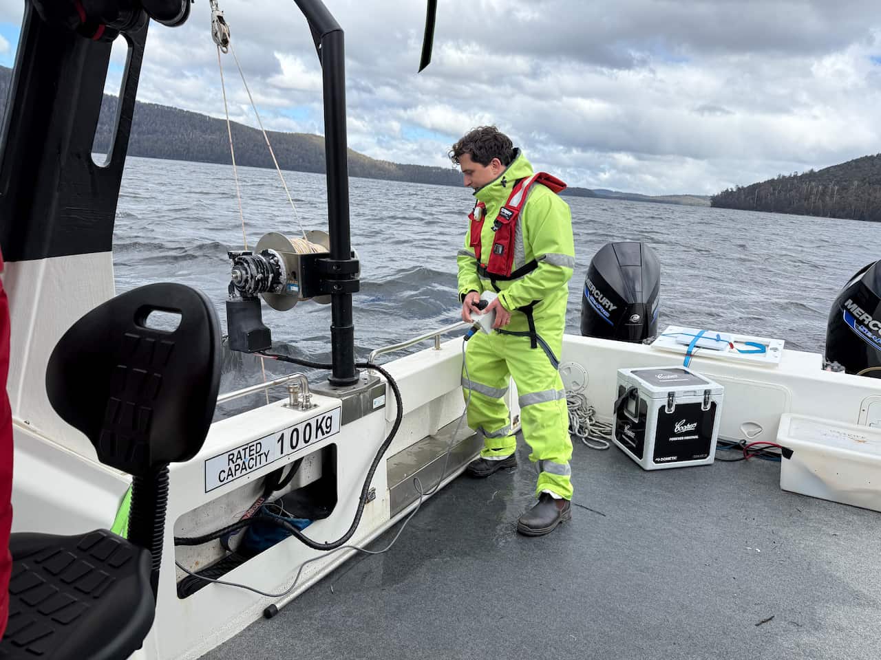 A man wearing a high yellow vis jump suit on a boat in a lake