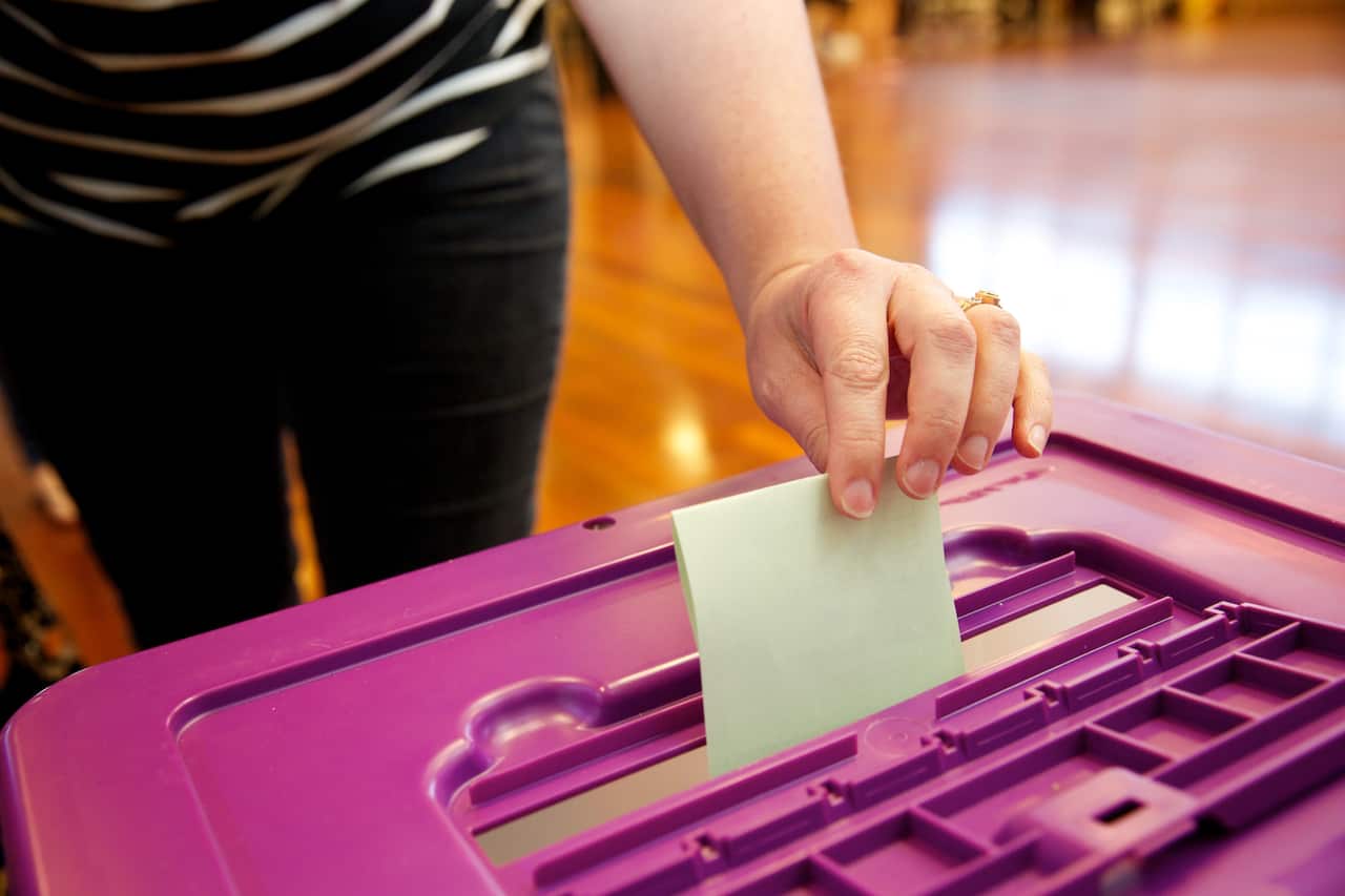 A woman slips a piece of paper into a voting booth slot.