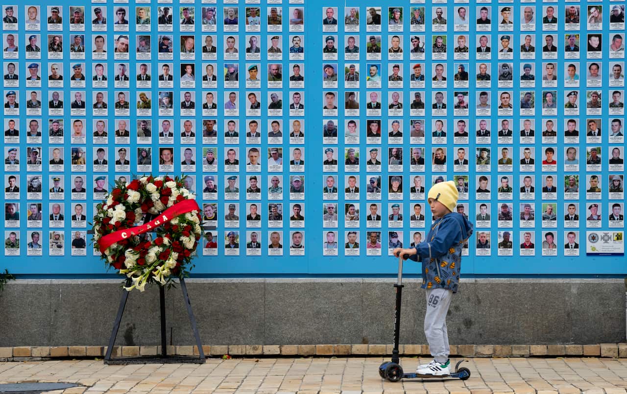 A child stands in front of a memorial showing pictures of Ukrainian soldiers who died