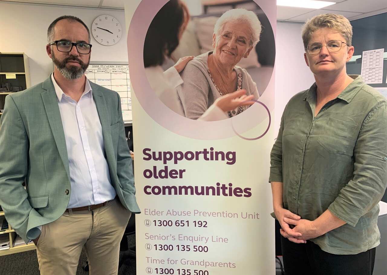Luke Lindsay and Deanne Lawrie stand in front of an elder abuse poster 