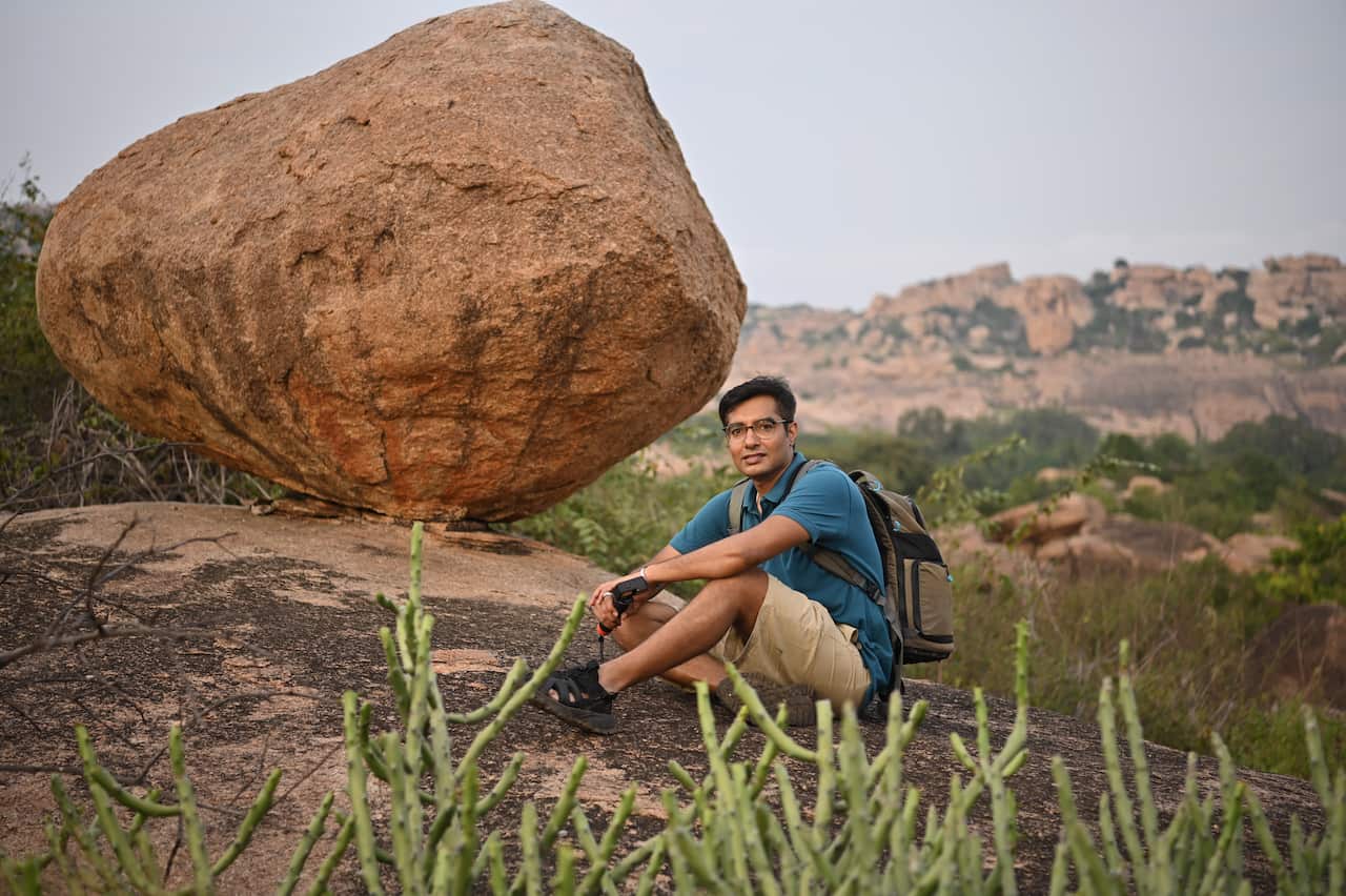 Portrait of a man sitting on rocks in front of huge Boulder and cactus