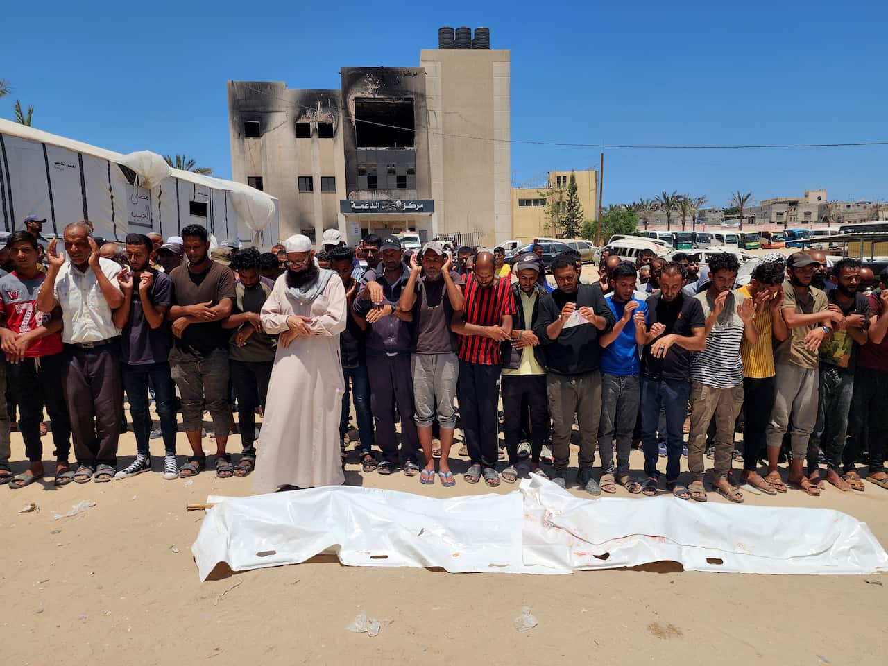 A crowd prays over the bodies covered under a long white sheet.