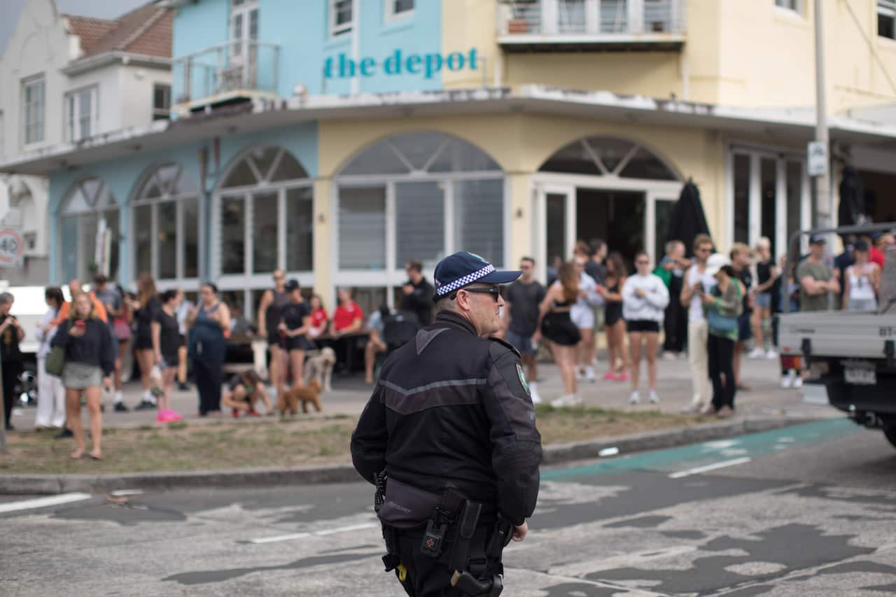 A large crowd of people gathered outside a building, while a police officer stands on the road.