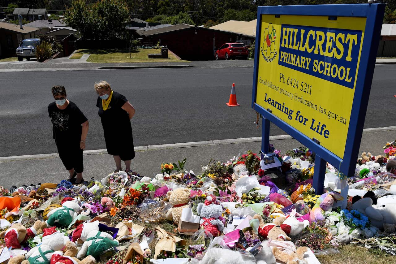 Two people looking at a memorial with flowers, teddy bears and other items. They are beneath a sign that reads: Hillcrest Primary School.