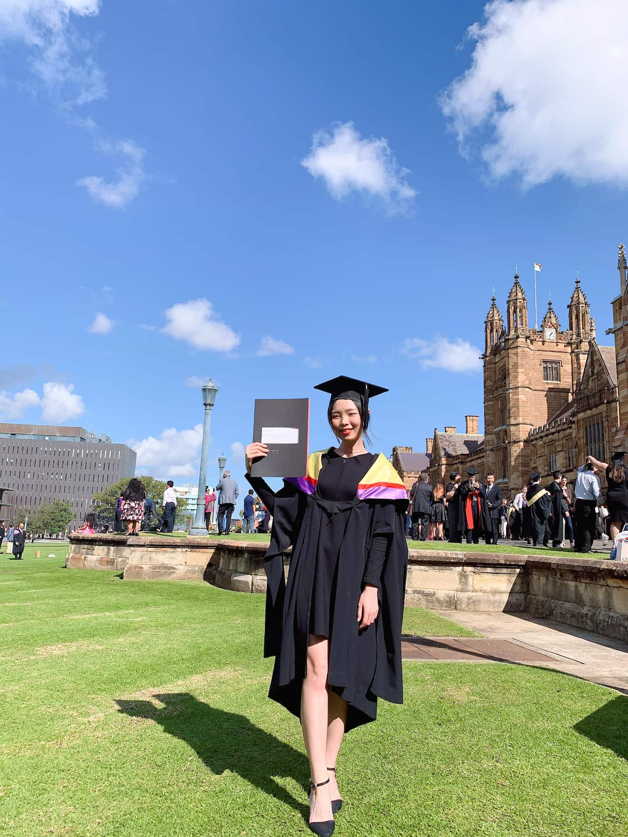 A woman in academic regalia poses in front of an old building.