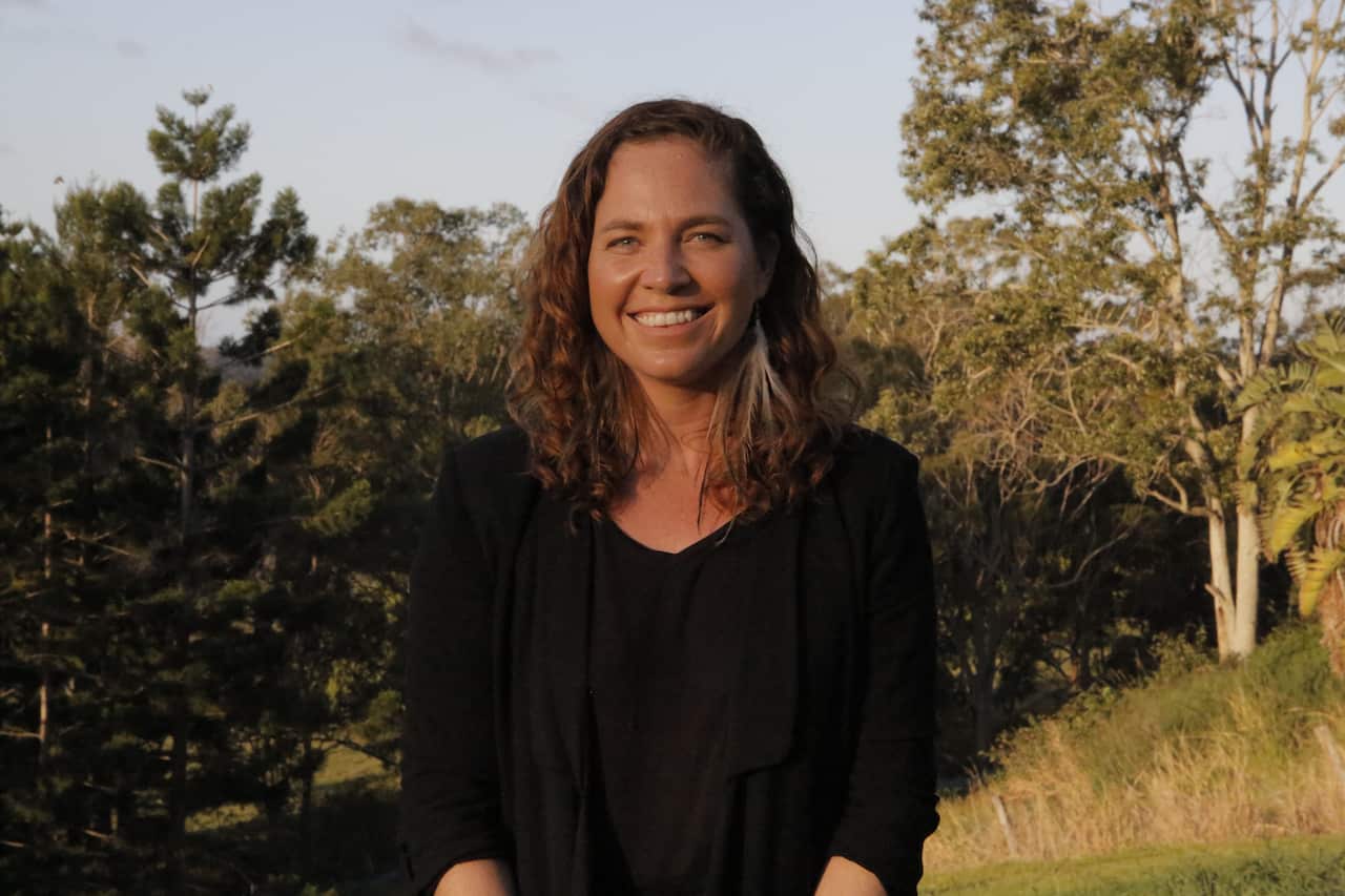A woman standing in the countryside smiles at the camera.