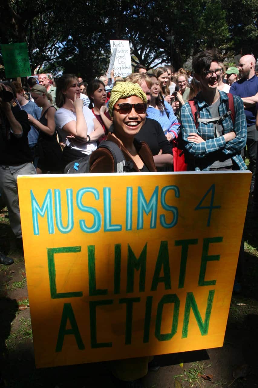 Fahimah stands outside behind a sign which reads: "Muslims 4 climate action". A group of people stand behind her.