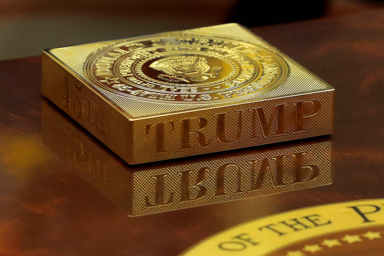 A shiny, gold, rectangular coaster with the word "TRUMP" engraved on its side and the US Presidential Seal on top.