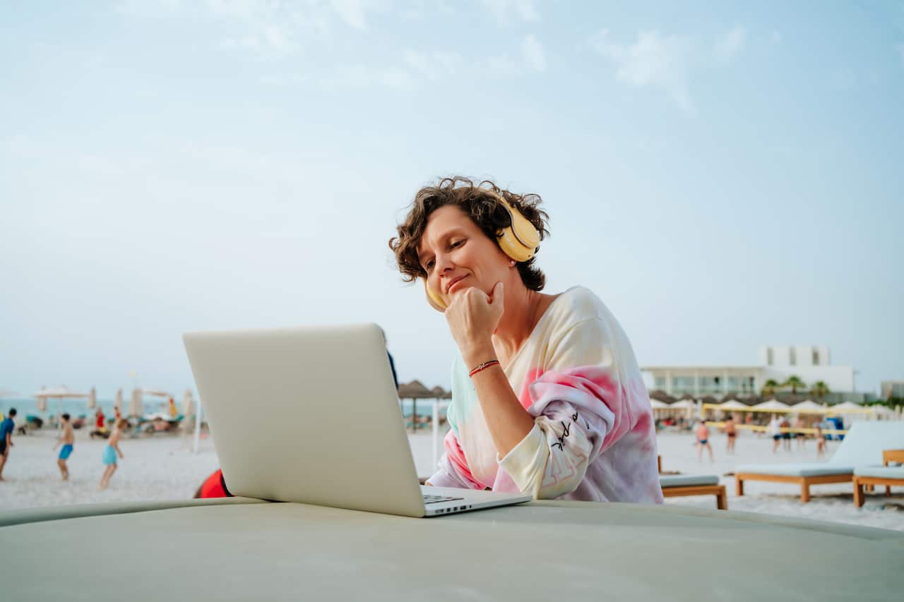 Smiling woman with wireless headphones enjoys the beach and video calls on the sunny beach