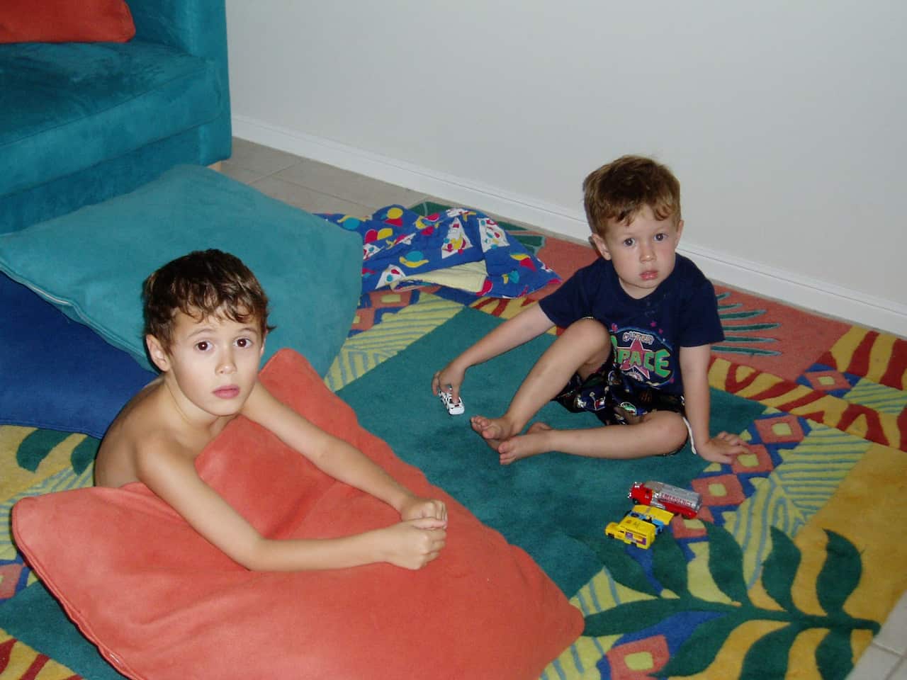 Two young boys sitting on a colourful rug. 