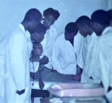 A group of nurses stand around a young boy in a clinic.