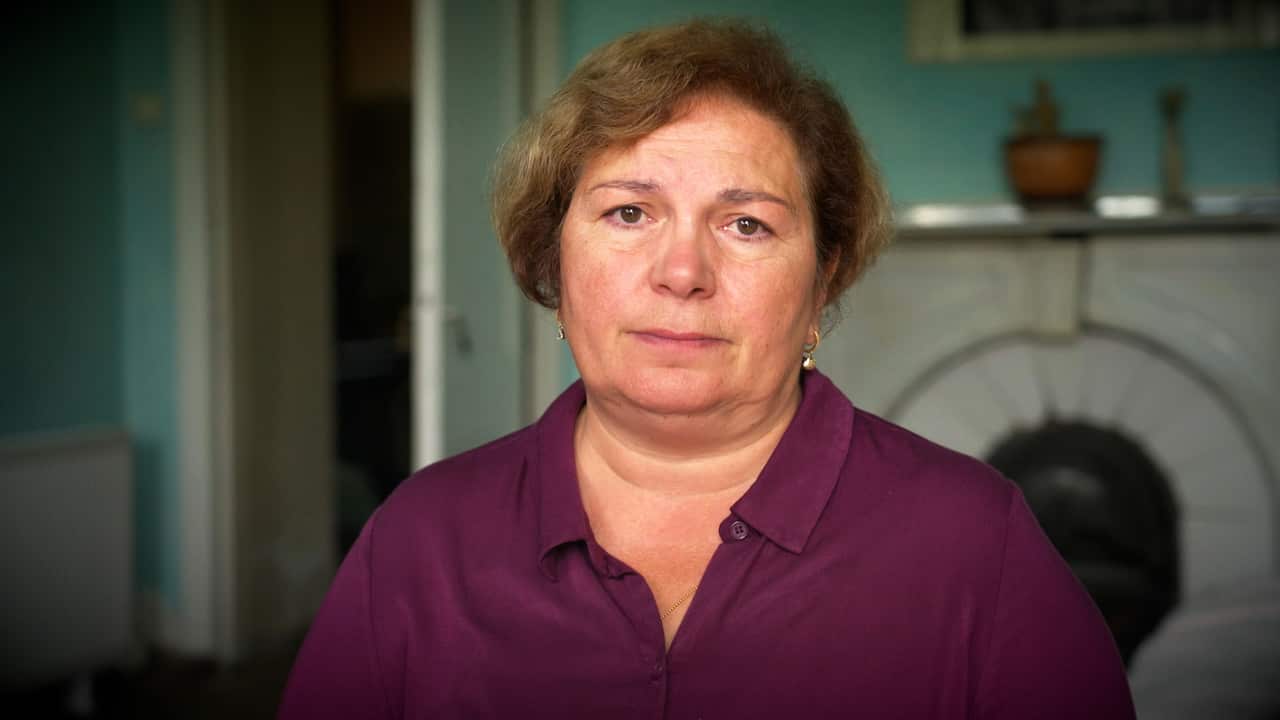 A middle-aged woman with short dark blonde hair wearing a burgundy shirt looks straight into the camera