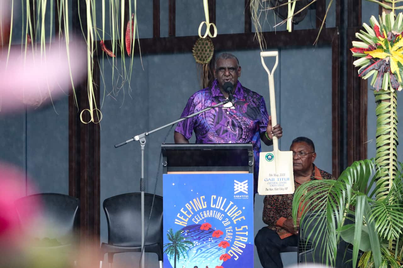 At the 20th celebration, Gabriel Bani spoke while holding the shovel his late father used to turn the soil.