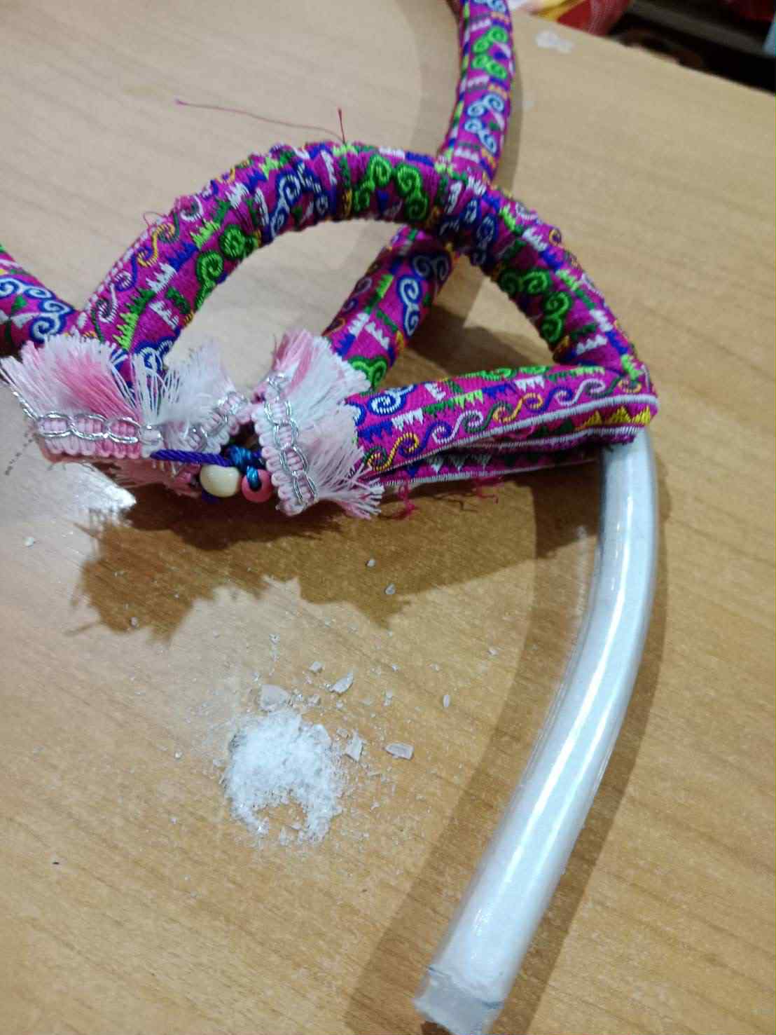 A brightly colored, fabric-wrapped tube, possibly part of a hookah hose, is shown cut open on a wooden surface, revealing white granular contents, with a small pile of the white substance next to it. 