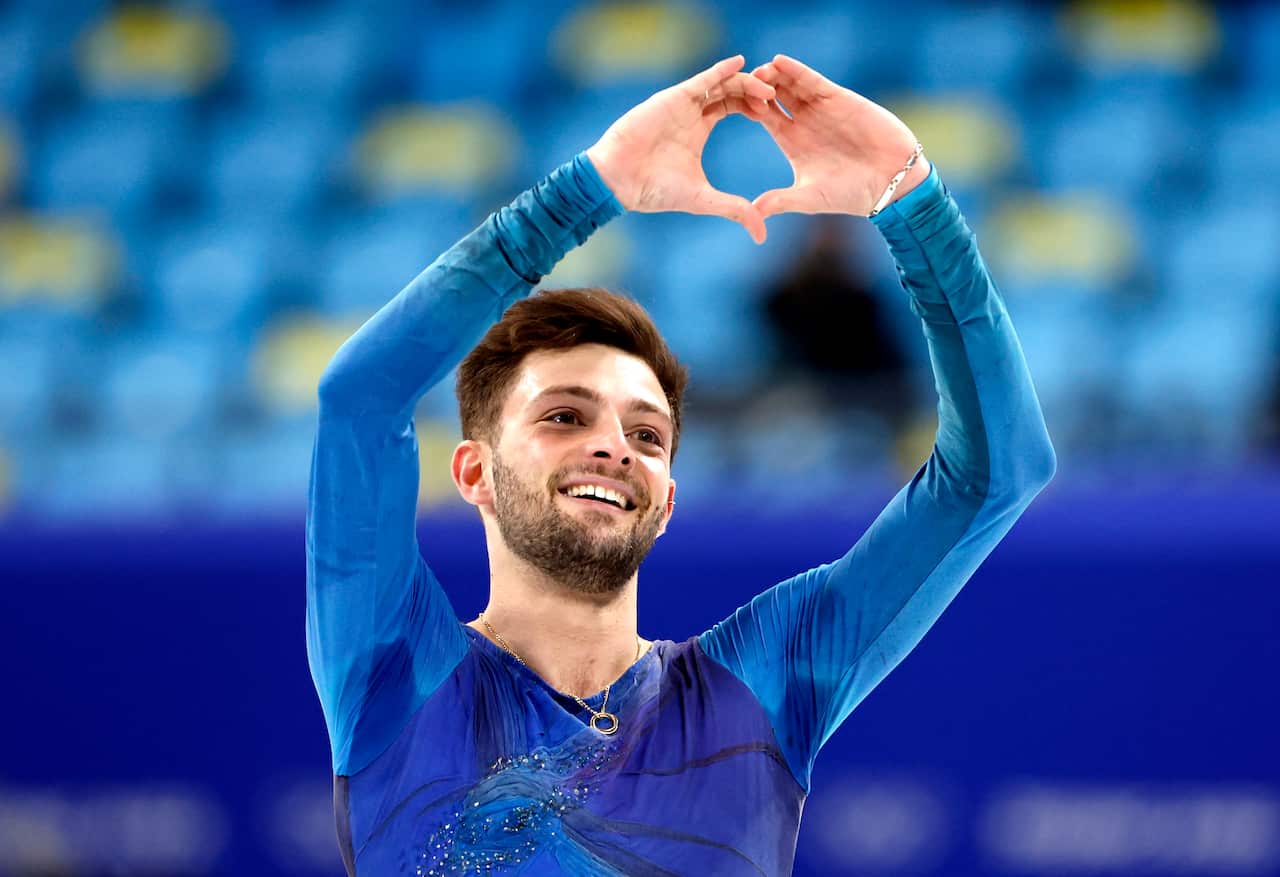 A man in blue gear making a heart sign with his hands in front of empty seats in an arena.