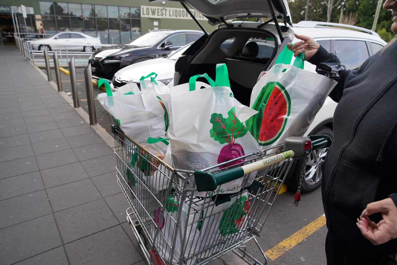 An arm picking up a grocery bag from a trolley to place into the back of a car.