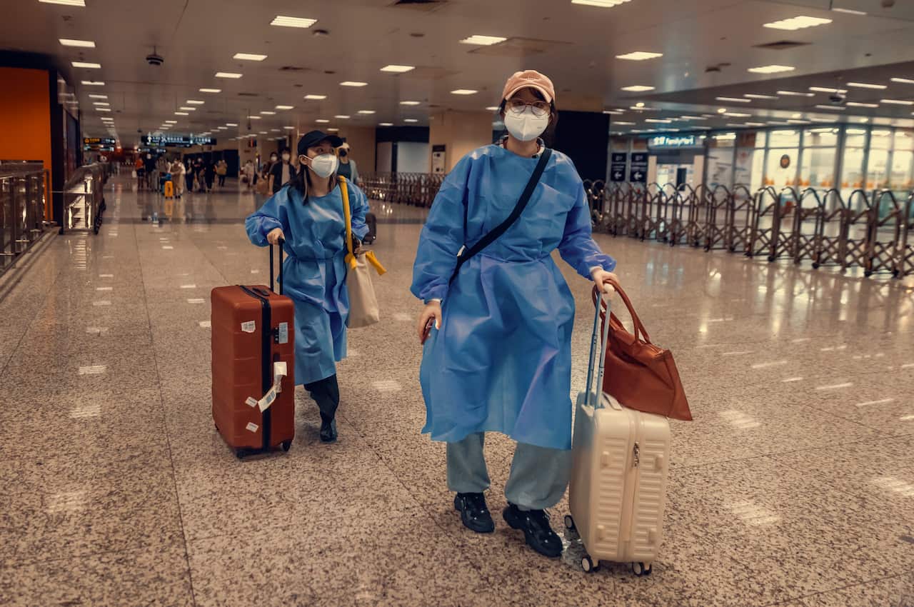 People wearing masks and gowns arrive with their luggage at Hongqiao railway station
