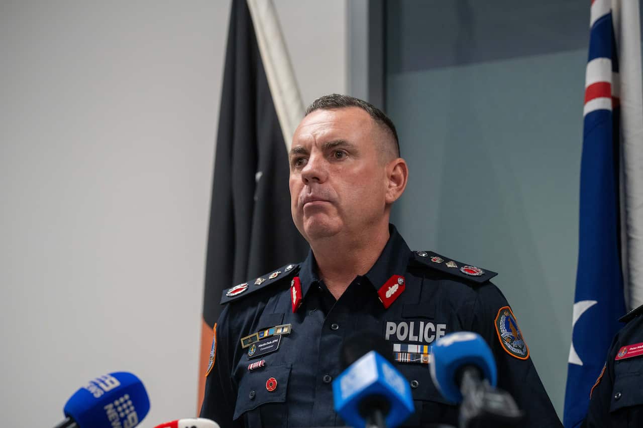 A man in a police uniform, speaking into media microphones.
