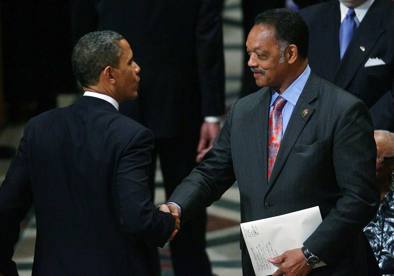 Barack Obama and Jesse Jackson, both wearing black suits and shaking each others' hand.