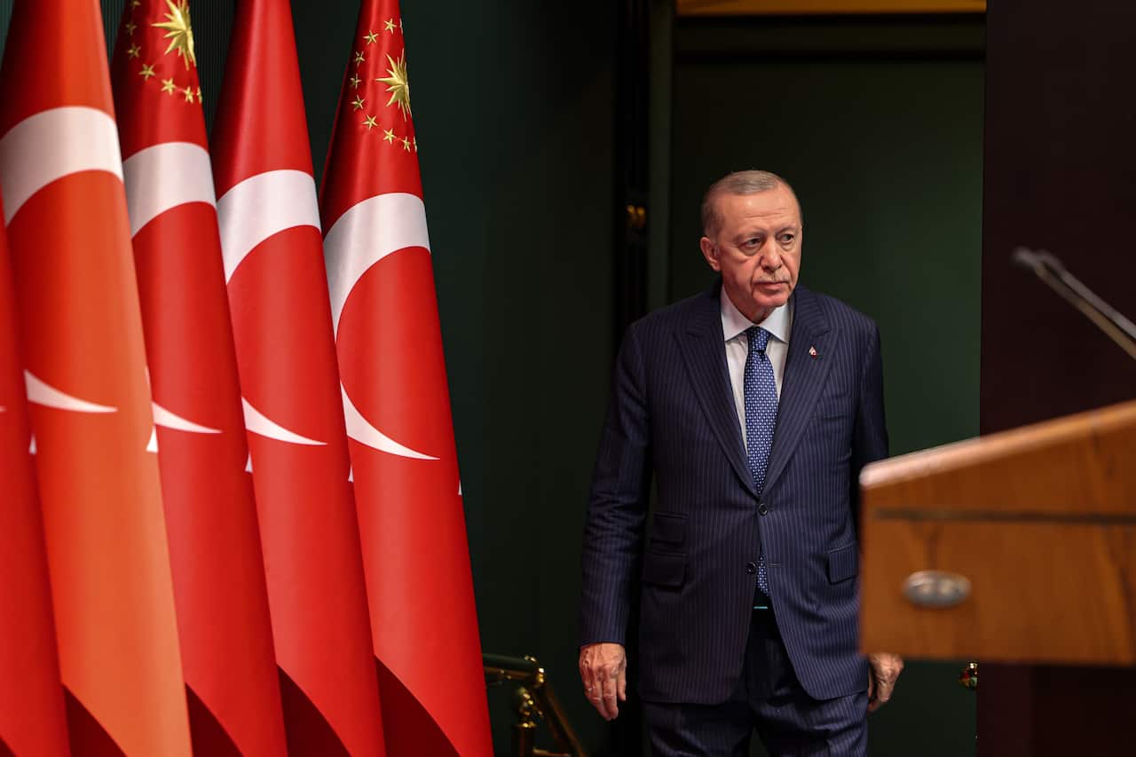 A man in a suit and tie walks towards a dais with Turkish flag in the background.