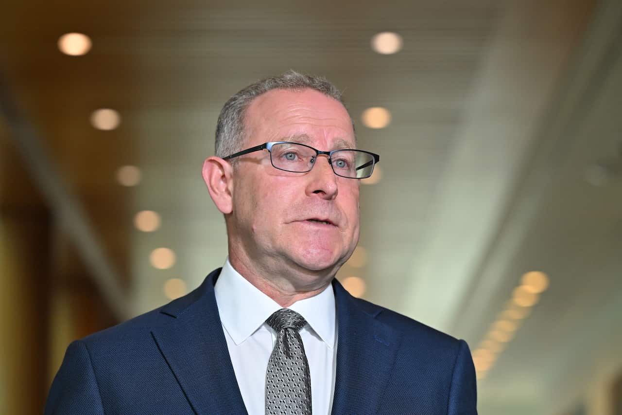 A middle-aged white man with short hair, wearing glasses, a navy suit and grey tie.