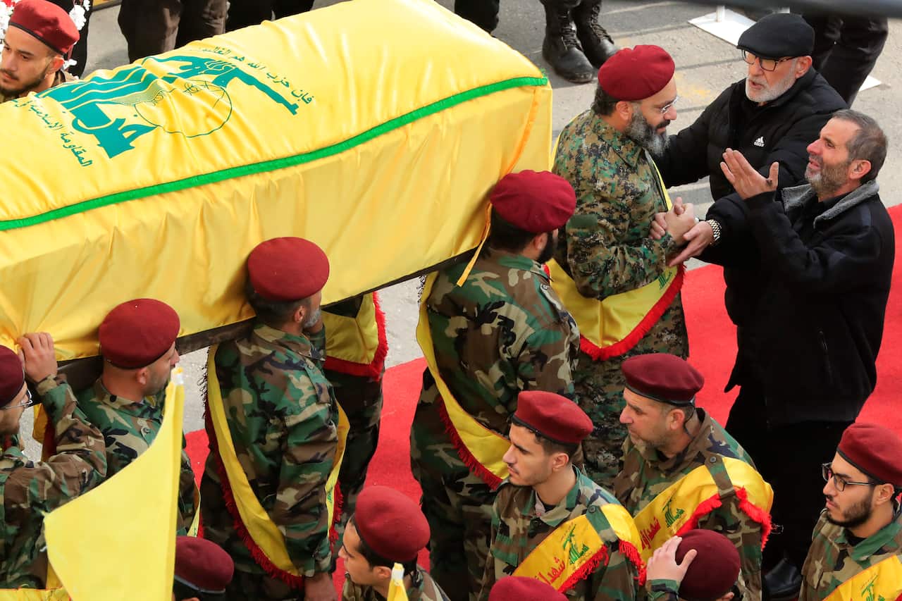 The funeral procession features the coffin being carried by individuals dressed in military uniforms.