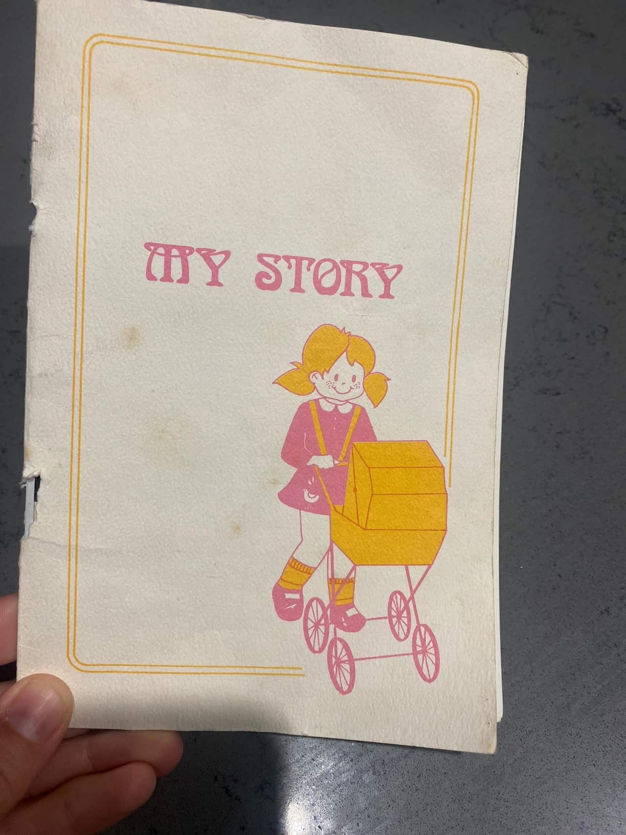 An old adoption booklet with a picture of a girl pushing a pram and the words 'My Story'.