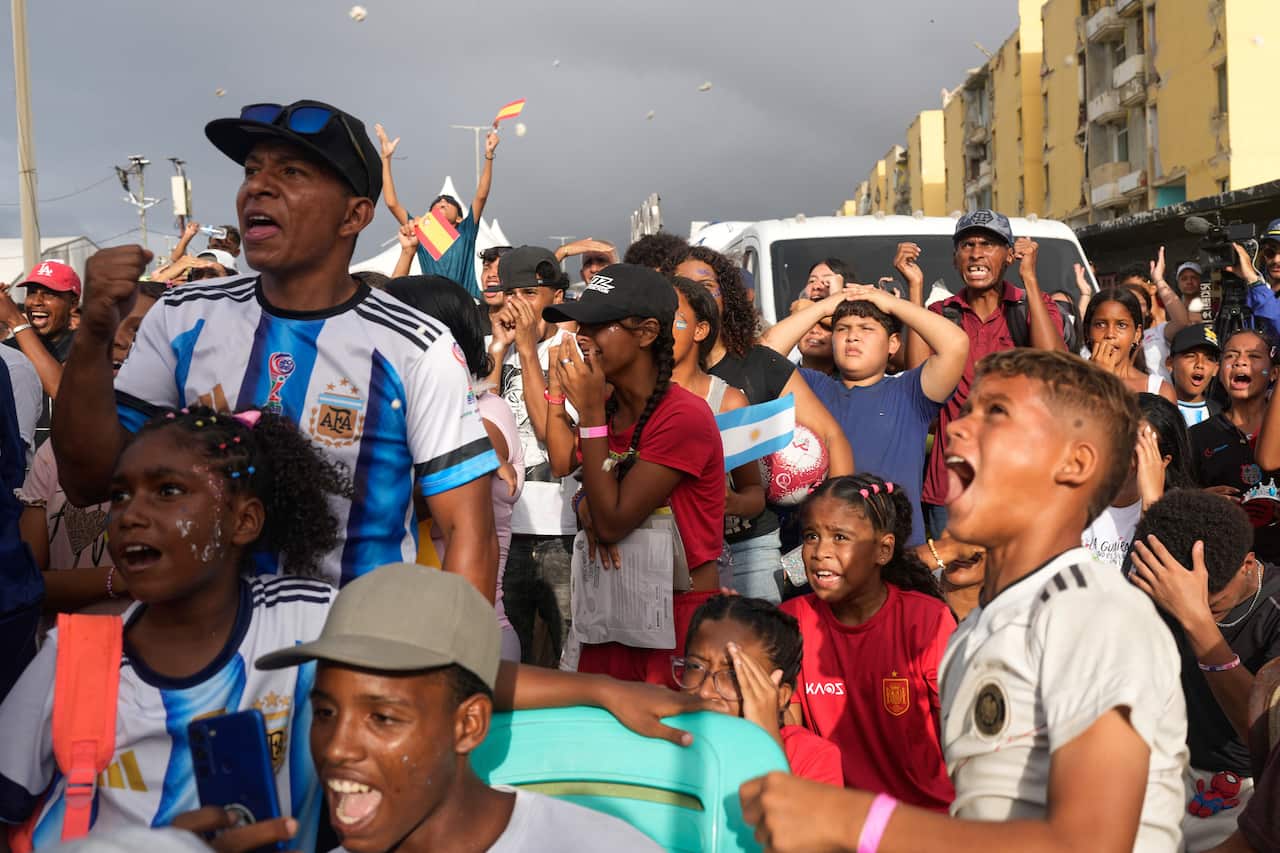 A large group of people standing outside, many of them wearing Argentina uniforms, cheering.
