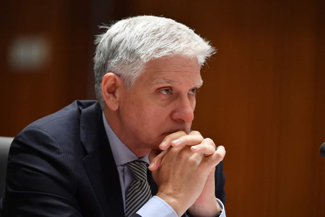 A man in a suit sitting with his hands clasped in front of his face.