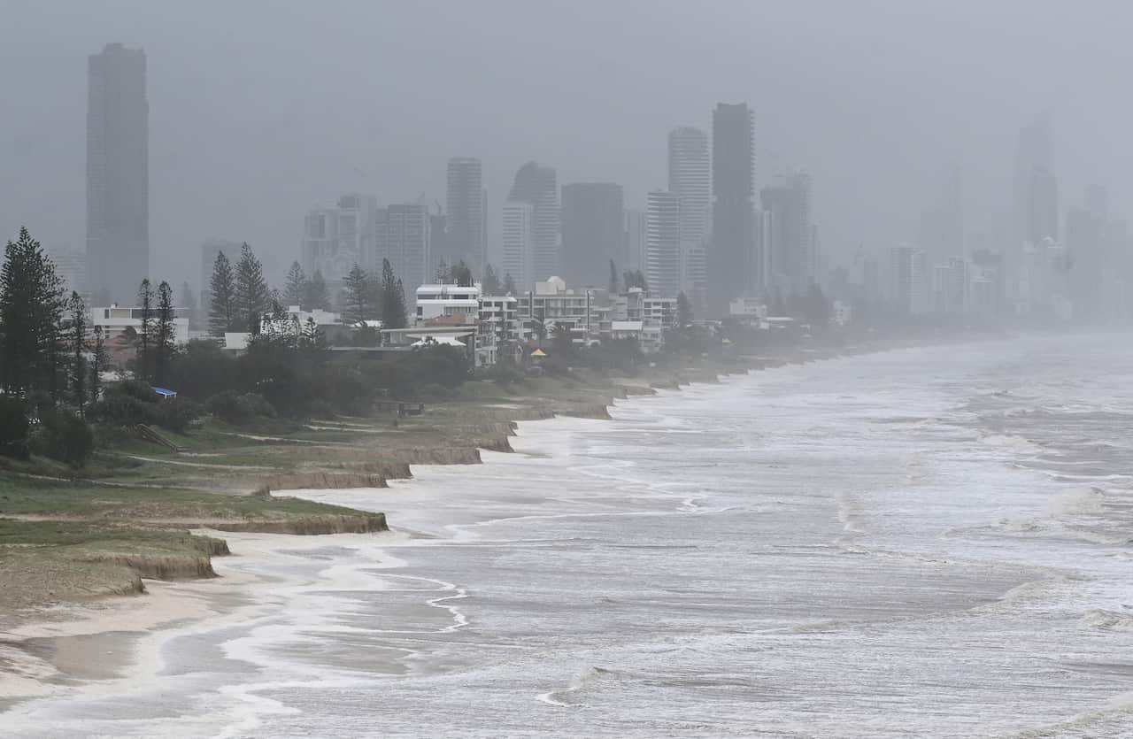 A wide shot of waves crashing into the shoreline with foggy apartment buildings in the background. 