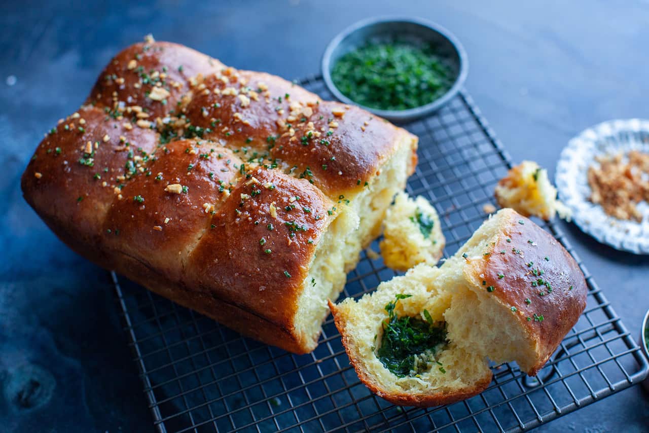 A golden tear-apart loaf sits on a cooling rack. The front quarter of the loaf has been torn off and sits in front, showing a green filing.
