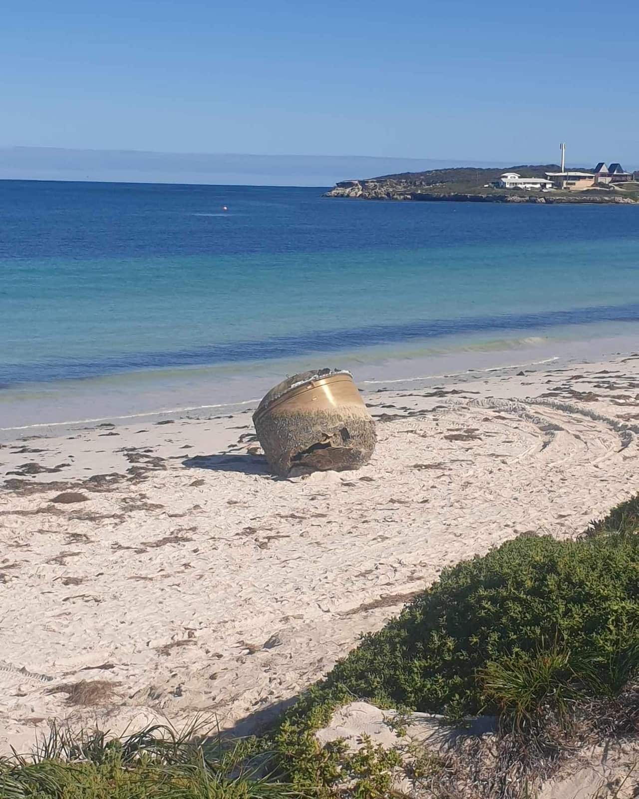 A large canister on the white sand of a beach with the ocean in the background.