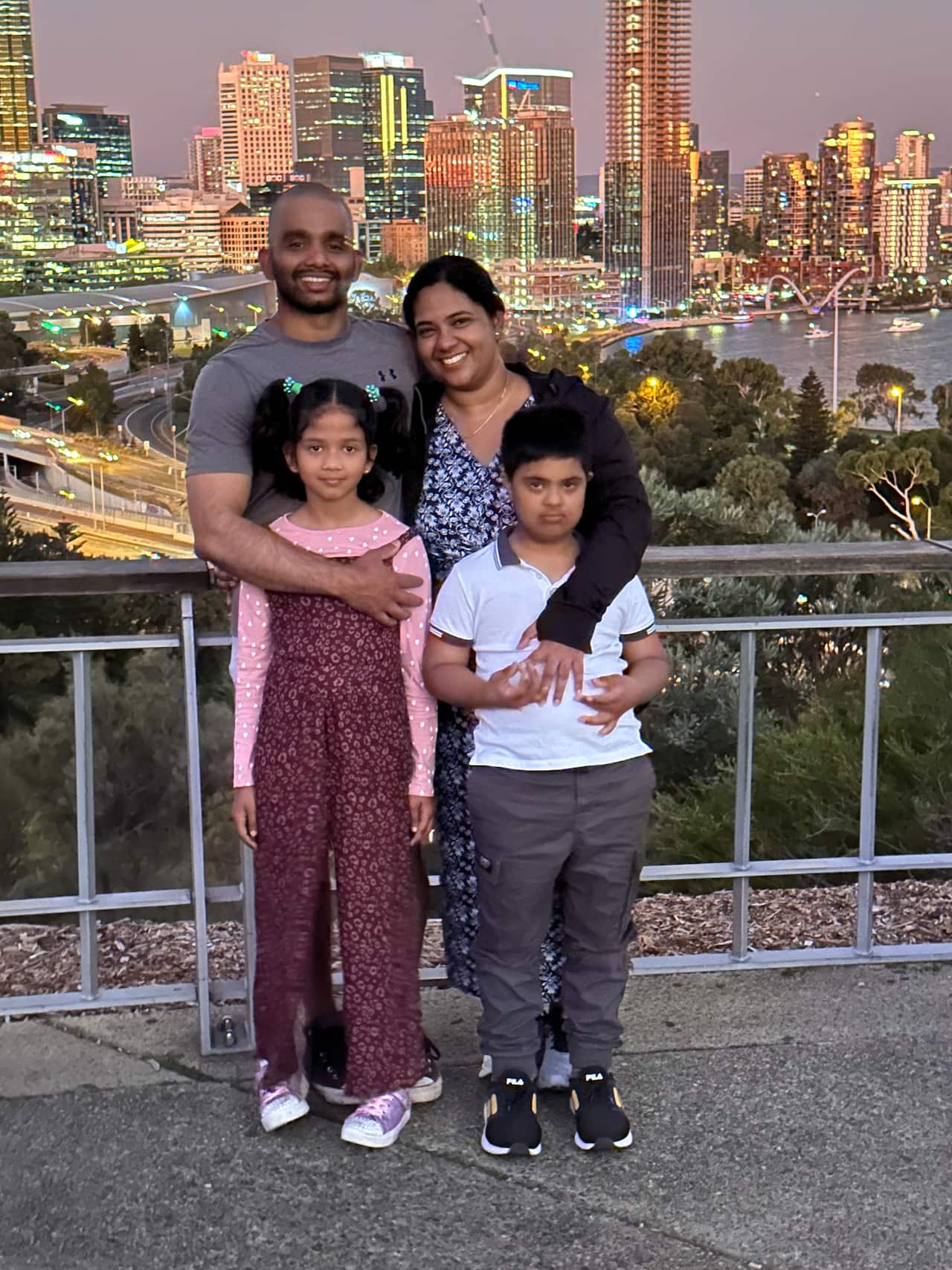 Two adults and their two children smile in front of a cityscape.