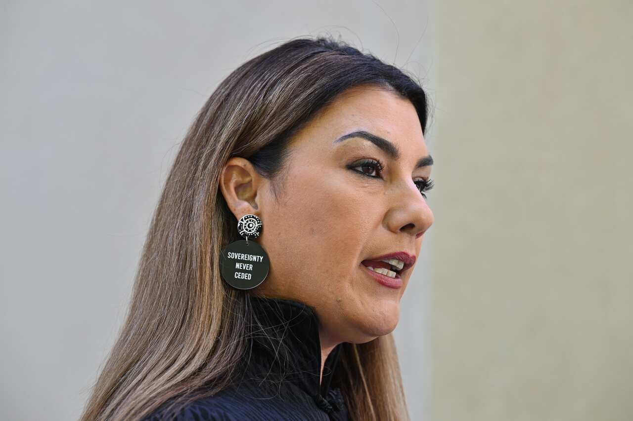 Side view of a woman with long dark hair. She has a black disc earring in her right ear that reads: Sovereignty never ceded