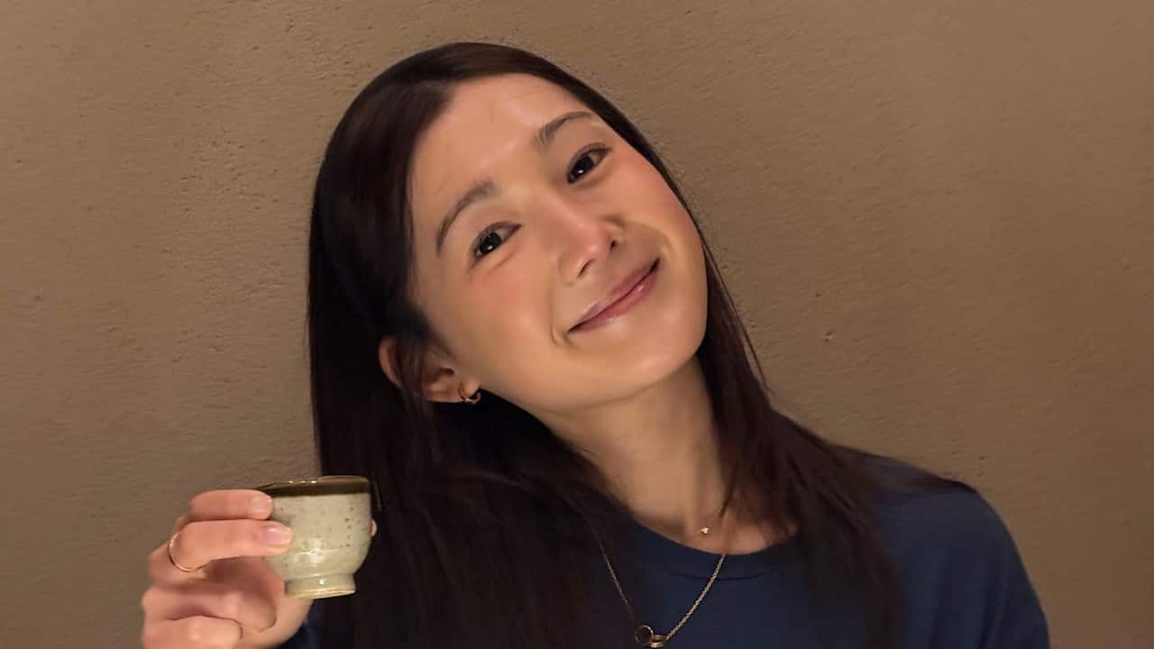a closeup of a young woman with long black hair in a navy sweatshirt, holding a cup of tea
