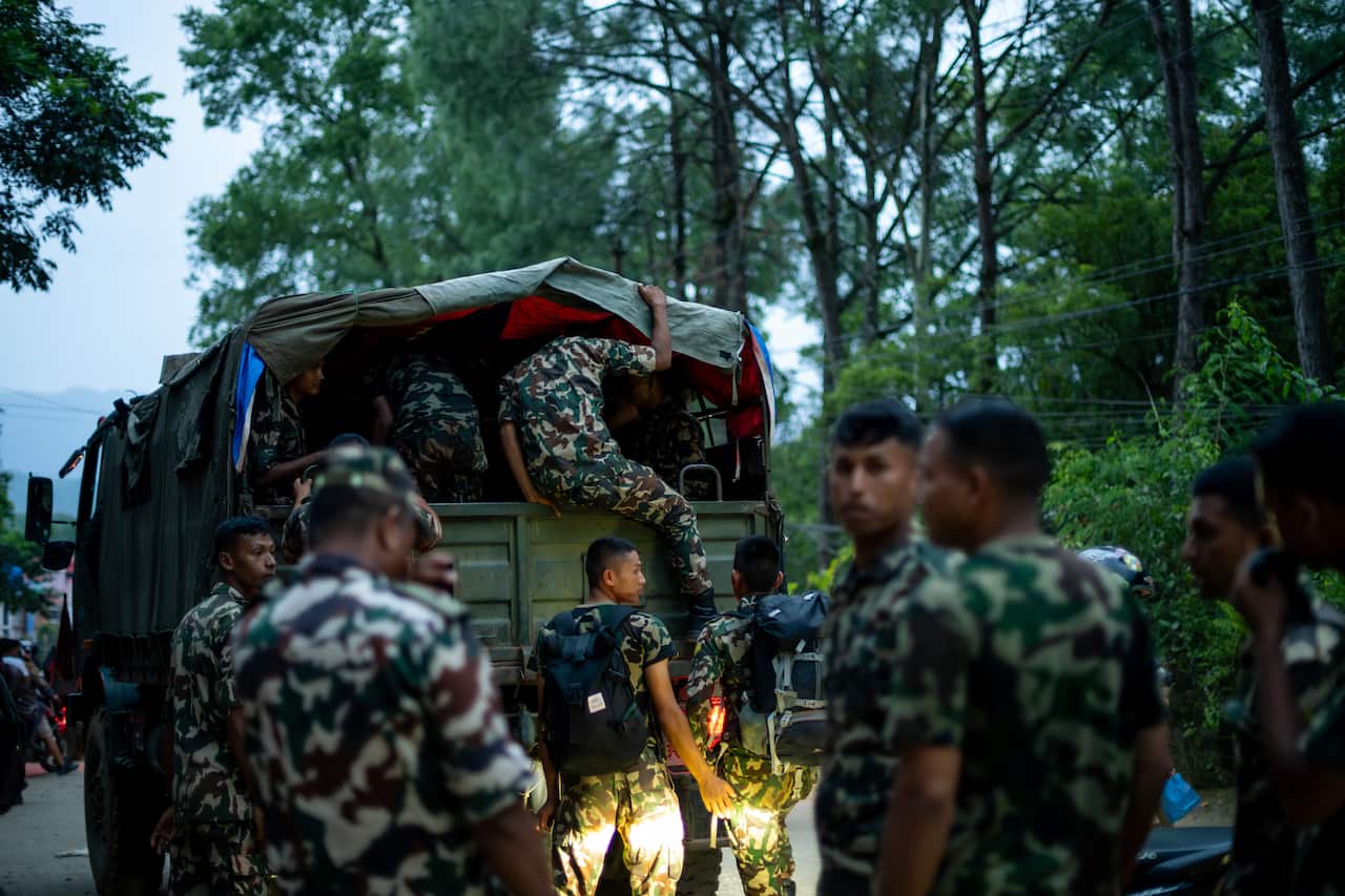 Soldiers in green military fatigues around a military truck, some people are inside in the back of it